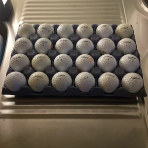 24 st titleist mix bollar - Bilderna visar en samling golfbollar av märket Titleist, prydligt placerade i en förvaringsbricka. Det finns ingen bok synlig på bilderna.