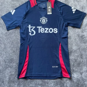 Manchester United tränings-tshirt Adidas - Snygg marinblå Manchester United tränings-tshirt från Adidas med röda detaljer vid axlar och sidor. Slim fit-modell i funktionsmaterial med klubbmärke och Tezos-tryck på bröstet. Perfekt för dig som vill visa ditt stöd på planen eller läktaren.