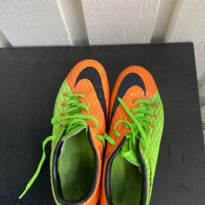 Nike Hypervenom fotbollsskor orange/grön Neymar  - Säljer ett par Nike Hypervenom fotbollsskor i en riktigt fet färgkombo av neonorange och neongrönt med svarta detaljer. Skorna har gröna snören, svart sula med gula dobbar och är tillverkade i syntetmaterial med textur för bättre bollkontroll.