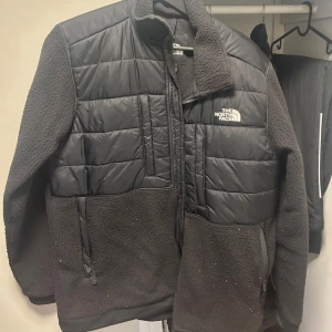 Svart fleecejacka från The North Face - Svart fleecejacka från The North Face med quiltade partier på bröst och rygg, dragkedja framtill och höga fickor. Jackan har långärmade ärmar och en clean, sportig look med broderad logga på bröstet. Perfekt för lager-på-lager och chill vardagsstil. Nypris 2000kr
