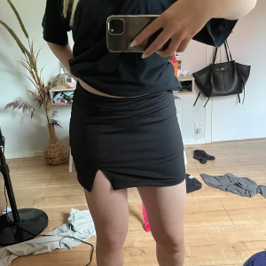 Svart kortkjol med slits - Säljer en svart tight kortkjol med liten slits framtill. Kjolen har inbyggda shorts under vilket gör den superbekväm och perfekt för dig som vill känna dig trygg när du rör dig. Enkel och stilren design som passar till många olika outfits. Skriv vid frågor❤️