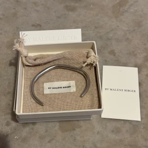 Silverfärgat armband By Malene Birger - Stilrent armband i 925 sterling silver  från By Malene Birger. Armbandet har en modern, böjd form och är tillverkat i metall med en blank finish. Perfekt för dig som gillar minimalistiska accessoarer med en cool touch. Levereras i originalask med tygpåse. Mjukt och formbart efter din handled! Använd men fortfarande mycket fint skick! Nypris: 3000kr