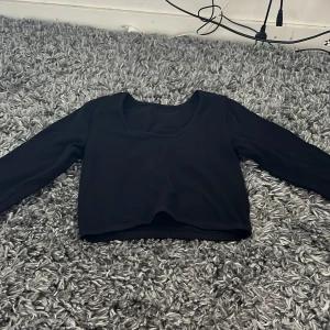 Svart ribbad croppad långärmad topp - En svart croppad topp med lång ärm och rundad urringning. Tyget är ribbat för en snygg struktur och sitter tajt mot kroppen. Perfekt att styla med höga jeans eller kjol för en clean look. Den är väldigt stretchig och passar upp till S 