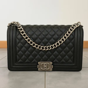 Svart quiltad  Boy Bag - Säljer en ikonisk svart  Boy Bag i quiltat skinn med grov silverfärgad kedja och klassiskt CC-spänne framtill. Väskan har en boxig form och lyxig känsla, perfekt för dig som vill ha en statementväska med exklusiv vibe.
