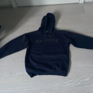Mörkblå hoodie med strass från Gina Tricot. - Mörkblå hoodie från Gina Tricot med texten 'MA CHÉRIE' i strass på bröstet. Tröjan har huva med snörning och långa ärmar. Perfekt för dig som gillar en enkel men ändå snygg look.