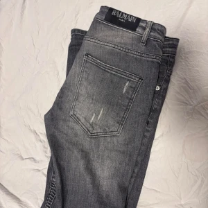 Grå bikerjeans från Balmain med dragkedjor - Snygga grå bikerjeans från Balmain med slitningar, ribbade detaljer vid knäna och coola dragkedjor framtill. Slim fit-modell med klassisk femficksdesign och en riktigt urban vibe. Perfekta för dig som vill sticka ut med en edgy streetstyle.