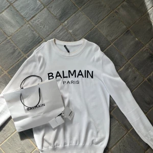 Balmain Paris tröja - Vit tröja från Balmain Paris med klassisk logga framtill. Självklart äkta ✅kvitto tillkommer🙏 Nypris: 6000 kr❗ Mitt pris: 3500 kr💸 Tröjan är i mycket bra skick (8.5/10), endast små defekter som syns på sista bilden 🔍 Stilren design i hög kvalitet  Hör gärna av dig vid frågor eller fler bilder!📩 