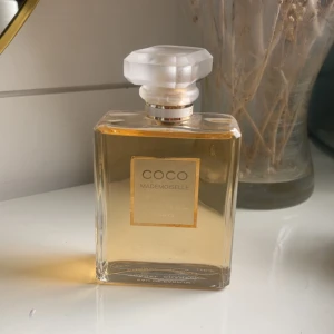 Chanel Coco Mademoiselle EdP 100ml - Chanel Coco Mademoiselle Eau de Parfum i klassisk, fyrkantig glasflaska med frostad, multifasetterad kork. Parfymen har en varm bärnstensfärgad vätska och elegant guldig etikett. En ikonisk doft från Paris som utstrålar lyx och stil.