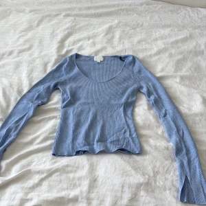 Ljusblå ribbad topp från H&M - Supersnygg ljusblå ribbad topp från H&M med lång ärm och figurnära passform. Djup rundringning och stretchigt material som sitter skönt. Perfekt att styla med jeans eller kjol för en chill look.