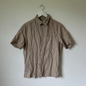 Beige kortärmad linneskjorta H&M - Snygg beige skjorta från H&M i regular fit med korta ärmar och klassisk krage. Skjortan har knäppning framtill och en bröstficka. Tillverkad i en luftig mix av linne och bomull, perfekt för varmare dagar. Artnr: A343