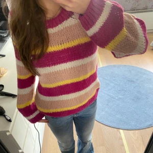 Färgglad stickad tröja - Superfin stickad tröja med breda ränder i rosa, beige, gult och vinrött. Tröjan har lång ärm och en avslappnad passform, perfekt för att liva upp vardagslooken.