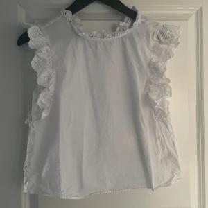 Vit blus med volang från H&M - Säljer en söt vit blus från H&M med volangdetaljer. Blusen är ärmlös och har en liten öppning bak i nacken. Perfekt för vår och sommar! Inte använd särskilt många gånger men det är tyvärr för liten för mig💓💓