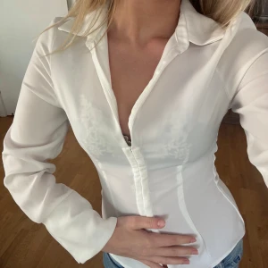 Vit figursydd skjorta från Zara - Säljer en vit, figursydd skjorta från Zara med klassisk krage och långa ärmar. Skjortan har knappar framtill och är tillverkad i ett slätt material som ger en stilren look. Perfekt att styla med jeans eller kjol.