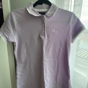 U.S. Polo Assn.  - Säljer en ljuslila pikétröja från U.S. Polo Assn. med vit krage och knappslå. Tröjan har korta ärmar och broderad logga på bröstet. Tillverkad i bomull med lite stretch för extra komfort. Har nästan aldrig använt den och köptes i USA för ungefär 700kr