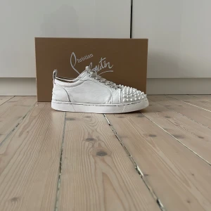 Vita sneakers med nitar från Christian Louboutin - Säljer ett par vita sneakers från Christian Louboutin, modell Vieira 2 Orlato Flat. och klassisk röd sula. med vita snören.