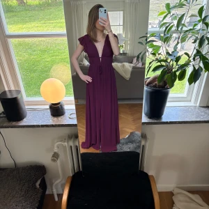 Långklänning i vinröd färg med volangärmar - Säljer en vinröd långklänning med djup v-ringning och volangärmar. Klänningen har öppen rygg och knyt i midjan för en snygg siluett. Perfekt för bal!!