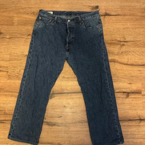 Levi's 501 jeans i klassisk blå denim - Klassiska Levi's 501 jeans i blå denim med raka ben och femficksmodell. Byxorna har knappgylf och läderpatch bak i midjan. Perfekta för dig som gillar tidlös stil och vill ha ett par ikoniska jeans.