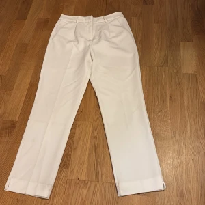 Vita kostymbyxor från KappAhl - Snygga vita kostymbyxor från KappAhl med klassisk rak passform. Byxorna har dragkedja och knäppning i midjan samt pressveck framtill. Perfekta för en stilren look.