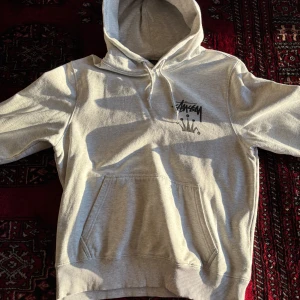 Grå hoodie från Stüssy med krontryck - Säljer en grå hoodie från Stüssy med svart logga och krona tryckt både fram och bak. Tröjan har huva och stor magficka. Super bra skick och Rare hoodie