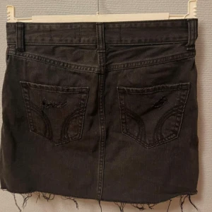 Svart jeanskjol med slitningar - Cool svart jeanskjol med slitna detaljer och fransig nederkant. Kjolen har klassiska fickor både fram och bak samt bälteshällor. Från Hollister storlek W25