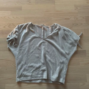 Ljusgrå topp med korta ärmar - Säljer en ljusrosa topp med lös passform och korta ärmar. Toppen har en rundad halsringning och är tillverkad i ett mjukt, strukturerat material. Perfekt för en avslappnad stil.