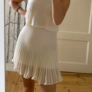 Vit  klänning från Topshop - Säljer en söt vit klänning från Topshop med plisserad kjol och ärmlös design. Klänningen har en luftig, lätt topp och rund halsringning. Perfekt för varma dagar och somriga tillfällen. Köpt i London för 46 pund. 