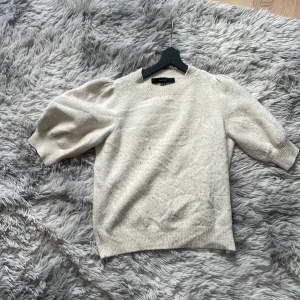 Beige stickad tröja med puffärm från Vero Moda - Säljer en beige stickad tröja från Vero Moda med puffärmar och rund halsringning. Tröjan har ribbade muddar vid ärmslut och nederkant, vilket ger en snygg och bekväm passform. Perfekt för lager-på-lager under kyliga dagar.
