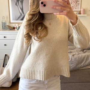 Beige stickad tröja med hög hals - Säljer en supermjuk och stilren beige stickad tröja med hög hals och långa ärmar. Tröjan har breda ribbade muddar vid ärmslut och nederkant, perfekt för lager-på-lager och en clean look.