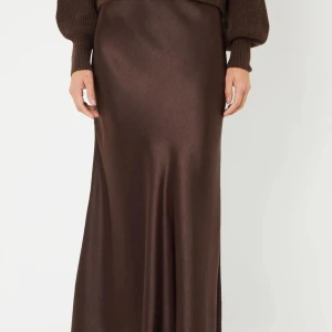 Brun långkjol i satin - Säljer en snygg brun långkjol i satin med lätt glansig finish. Kjolen har en rak och elegant siluett som faller fint längs benen. Perfekt nu till sommaren. Slits på sidan. BikBok storlek xs