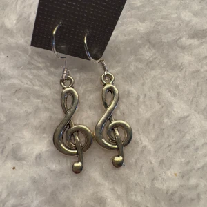 Silvriga örhängen med G-klav - Säljer ett par coola örhängen i form av G-klavar i silverfärg. Perfekta för dig som älskar musik och vill ha något unikt till din stil. Hängande modell med krok.