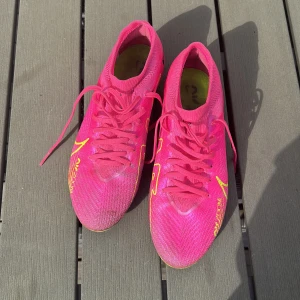 Nike Air Zoom Mercurial fotbollsskor i rosa - Säljer ett par Nike Air Zoom Mercurial fotbollsskor i en riktigt snygg rosa färg med gula och svarta detaljer. Skorna har snörning och är designade för att ge bra grepp på planen. Perfekta för dig som vill sticka ut på fotbollen!