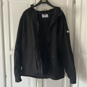 Svart jacka med huva från Weekend Offender - Säljer en svart jacka från Weekend Offender med huva och dragkedja. Jackan har en enkel och stilren design, perfekt för vardagsbruk. Materialet är syntet och jackan har långa ärmar samt praktiska fickor. Helt oanvänd. 