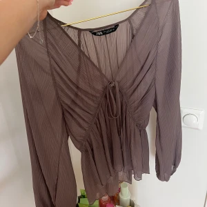 Plisserad brun blus från Zara - Populär slutsåld blus från zara, i en lila grå färg. Är inte lika genomskinlig som den framkommer på bild 2! Använd några gånger 