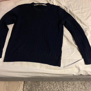 Mörkblå stickad tröja från Jack & Jones - Säljer en mörkblå stickad tröja från Jack & Jones Premium. Tröjan har rund halsringning och ett diskret kabelstickat mönster. Perfekt för lager-på-lager och passar till många olika stilar.