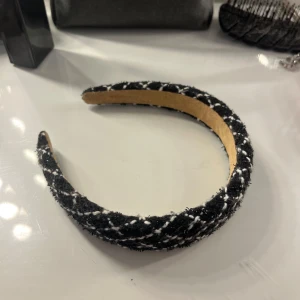 Svart och vit rutigt diadem - Snyggt diadem i svart tyg med vita rutor. Diademet har en vadderad känsla och är klätt i ett mjukt material som ger en trendig look. Perfekt accessoar för att lyfta din outfit.