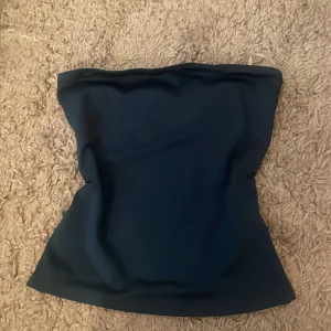 Mörkblå tubtopp - Säljer en enkel och stilren mörkblå tubtopp. Perfekt att matcha med jeans eller kjol för en snygg look. Toppen är ärmlös och har en slät yta utan mönster eller detaljer.