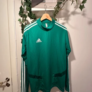 Långärmad adidas tröja - Väldigt cool grön adidas tröja, kan användas för sport eller bara stylad med något trevligt. Den är grönare i verkligheten. Klövergrön typ men reflekteras konstigt i kameran. Den har två streck som syns på tredje bilden annars bra skick. Sitter tajt, som en compression shirt. 
