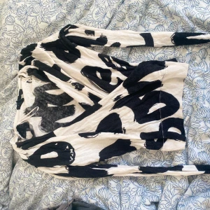 Svartvit omlottopp från Lindex - Säljer en svartvit omlottopp från Lindex med coolt abstrakt mönster. Tröjan har lång ärm och djup v-ringning. Materialet känns mjukt och stretchigt, perfekt för våren 🥰