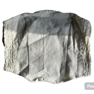 Vit tubtopp med dragkedja - Säljer en vit tubtopp med dragkedja bak och smockade sidor. Toppen har en enkel och stilren design, perfekt att matcha med jeans eller kjol. Materialet känns mjukt och bekvämt mot huden.