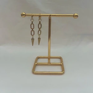 Guldiga kedjeörhängen med spetsig detalj - Säljer ett par trendiga örhängen i guld med kedjelänkar och en spetsig, konformad detalj längst ner. Perfekta för dig som gillar statement-smycken och vill sticka ut med din stil.