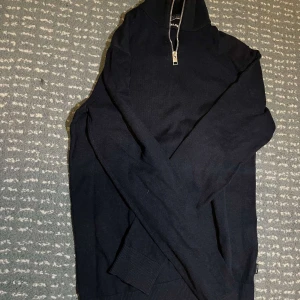 Mörkblå halvzip-tröja från Jack & Jones - Säljer en mörkblå långärmad tröja från Jack & Jones med halv dragkedja vid halsen. Tröjan har ribbade muddar och är perfekt för lager-på-lager. Enkel och stilren design som passar till det mesta.