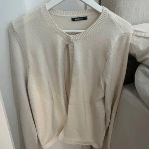 Beige kofta från Gina Tricot - Säljer en enkel och stilren krämfärgad kofta från Gina Tricot. Koftan har rund halsringning, lång ärm och knäppning längst upp. 