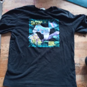 Svart t-shirt med spelmotiv från H&M - Cool svart t-shirt från H&M med ett färgglatt spelmotiv på framsidan. Perfekt för gaming-entusiaster! Kortärmad och tillverkad i mjukt material för bekväm passform.