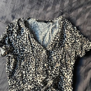 Leopardmönstrad blus från Vero Moda - Snygg leopardmönstrad blus från Vero Moda med knappar framtill och knytning i midjan. Blusen har korta ärmar och en v-ringad design. Sparsamt använd. Bra passform men för liten för mig.