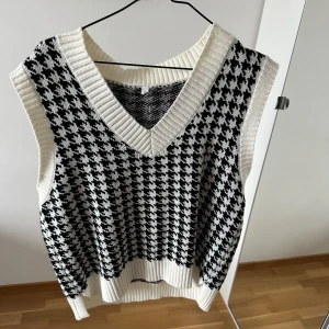 Svartvit stickad väst - Snygg svartvit stickad väst med ett klassiskt hundtandsmönster. Den har en v-ringad design och ribbade kanter som ger en stilren look🫶🏼