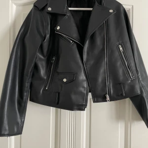 Svart skinnjacka från Zara - Snygg svart skinnjacka från Zara med dragkedja och knappar. Dock saknas skärpet som ska sitta i