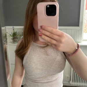 Beige ribbad linnetopp - Säljer en stilren beige ribbad linnetopp. Perfekt för varma dagar med sin ärmlösa design och mjuka material. Passar till både jeans och kjol för en avslappnad look.