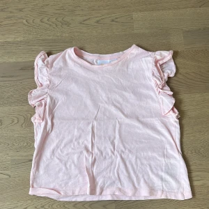 Rosa topp med volangärmar från Gina Tricot - Söt rosa topp från Gina Tricot med volangdetaljer på ärmarna. Perfekt för en avslappnad och stilren look. Tillverkad i mjukt material för extra komfort.