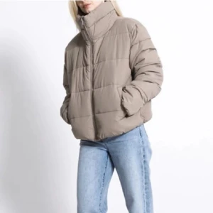 Beige pufferjacka från Lager 157 - Säljer en snygg beige pufferjacka från Lager 157. Jackan har en hög krage och dragkedja framtill. Perfekt för kyliga dagar med sin vadderade design. Den är långärmad och har en modern look. Passar perfekt för höst och vinter.