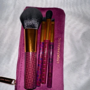 Sminkborstar med lila fodral från Lookfantastic - Set med fyra sminkborstar i olika storlekar med lila och guld detaljer. Borstarna kommer i ett snyggt lila fodral med dragkedja. Perfekt för att applicera både puder och ögonskugga.